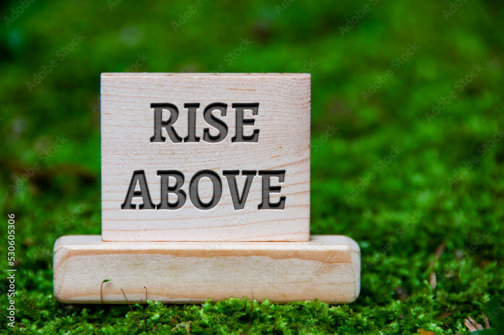 Rise above text on wooden block with green nature background. Motivational concept