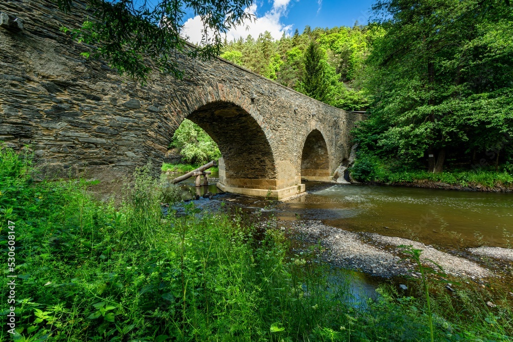 Rabstejn nad Strelou, Czech Republic - June 12 2022: View of the historical sandstone bridge over the river Strela made in the 14th century, a second oldest in the Czech Republic. Sunny summer day.