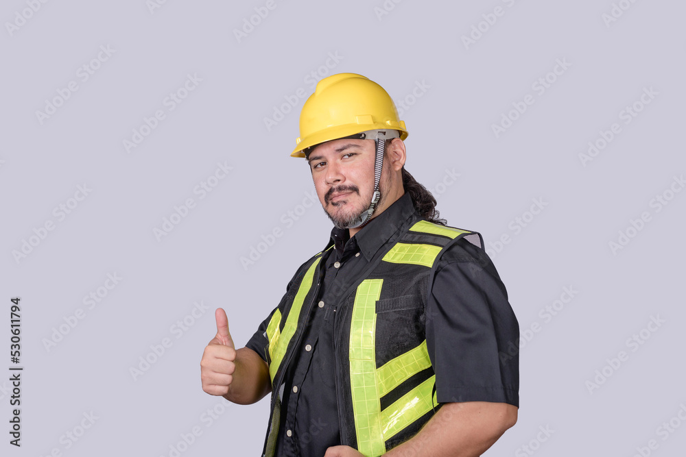 A burly foreman or engineer wearing a hardhat and safety vest gives a thumbs up of approval. Isolated on a gray background. A burly foreman or engineer wearing a hardhat and safety vest gives a thumbs up of approval. Isolated on a gray background.