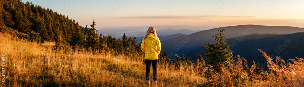 Woman looking at mountain range in natural parkland Jeseniky during sunset. Panoramic landscape with hiking tourist
