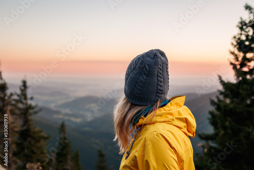 Woman with knit hat and yellow jacket looking at mountain range during sunset. Relaxation during hiking in mountains photo