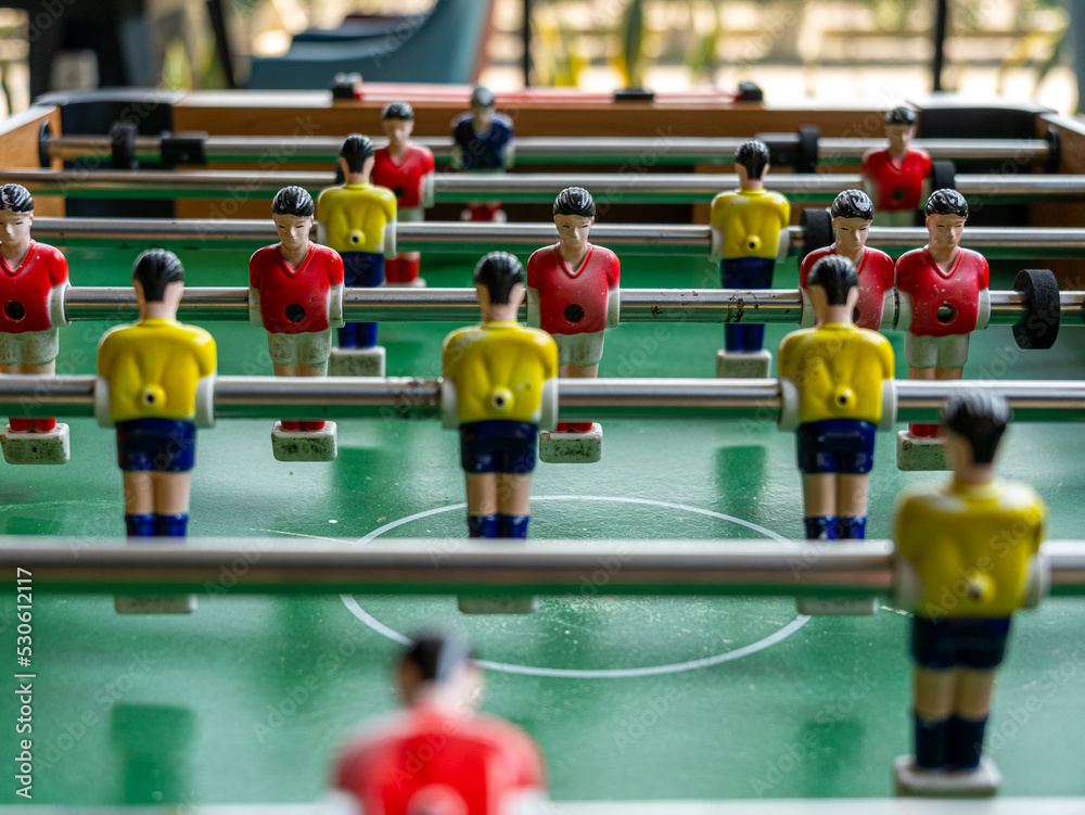A vertical close-up view of a typical foosball table with red and yellow dummies over a green surface simulating a soccer field. A vertical close-up view of a typical foosball table with red and yellow dummies over a green surface simulating a soccer field.
