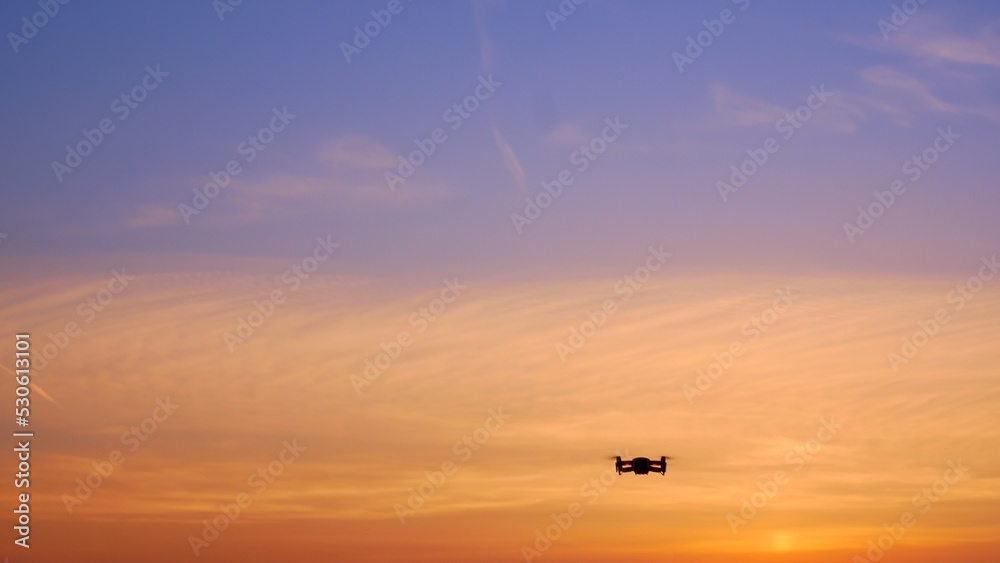 The drone takes off into the sunset sky over an unrecognizable place. A beautiful sky filled with sunset colors in which a drone flies with blinking lights. Four propellers lift the drone into the air