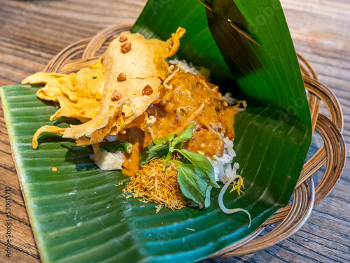 A traditional Nasi Pecel of Indonesia, consisting of steamed rice with assortment of boiled vegetables, a peanut cracker, and is covered by spicy peanut sauce, served on a banana leaf. photo