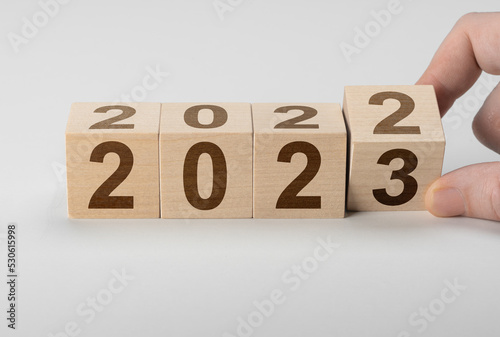 Wooden cube flipping, change from 2022 to 2023. Man hand flipping cubes with year 2022 to 2023. new year concept. Hand holding wooden cube with flip over block 2022 to 2023 word on gray background