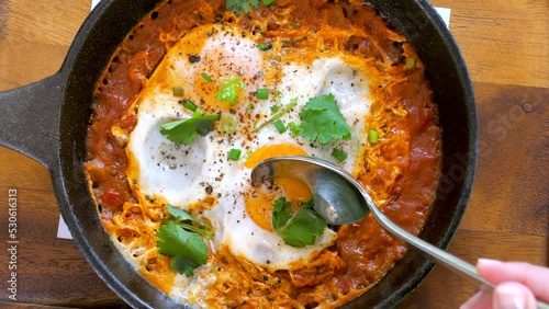 Woman hand take a Shakshouka or shakshuka from iron pan photo