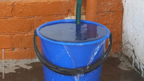 The water from the hose has filled the bucket and is overflowing