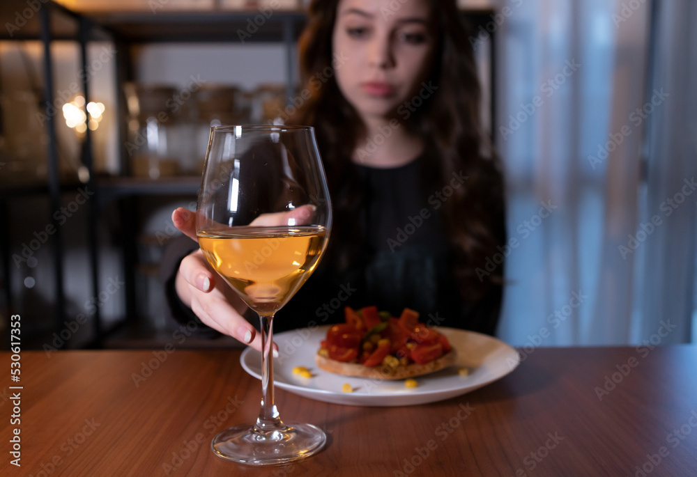 Young woman sitting in the kitchen with a glass of wine. Teen alcoholism concept, alcohol addiction problems among women Young woman sitting in the kitchen with a glass of wine. Teen alcoholism concept, alcohol addiction problems among women