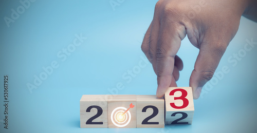 A hand man flip wood cubes with 2022 to 2023 on blue background. Start up of the new year 2023 beginning new year, new lifestyle, new normal, new business, setting target, and planning goals concept.