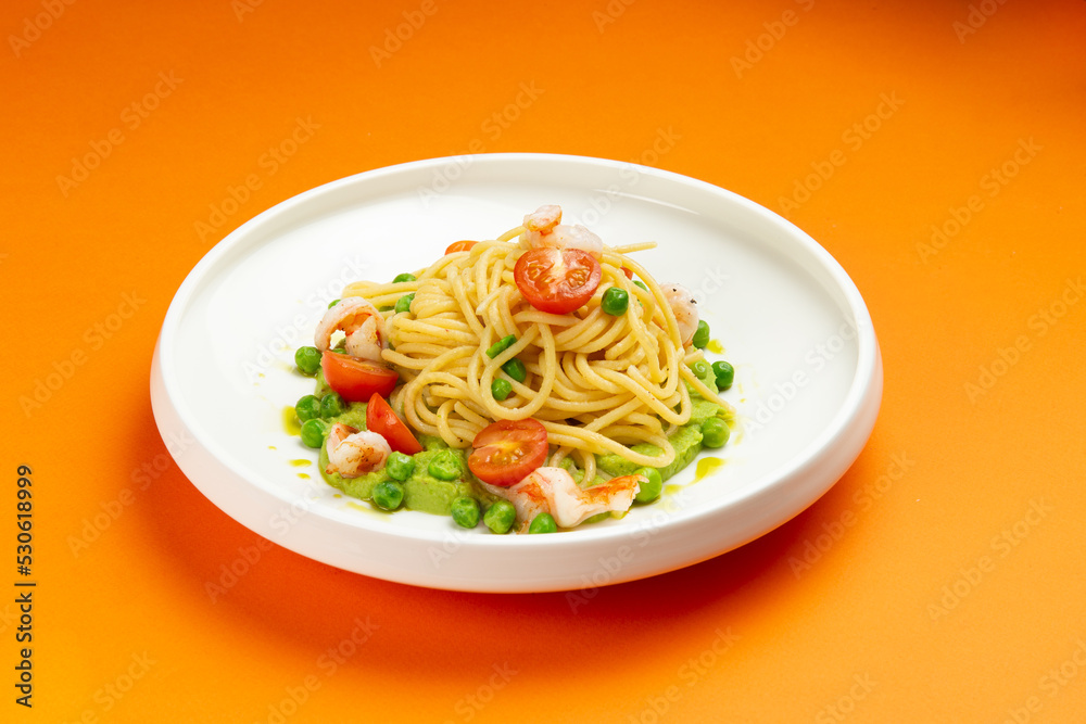Pasta with shrimp and tomato in a plate on an orange background.