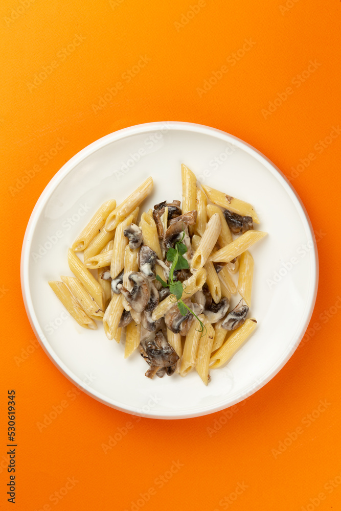 Pasta with mushrooms in a plate on an orange background. Pasta with mushrooms in a plate on an orange background.