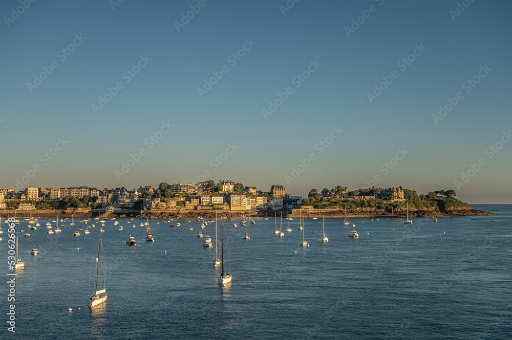 St. Malo, Brittany, France - July 8, 2022: Wide landscape over Rance river water to Pointe du Moulinet on peninsula with its many buildings under blue sky. English Channel behind. Yachts up front