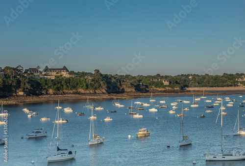 St. Malo, Brittany, France - July 8, 2022: White yeachts on blue Rance river mouth water in front of upscale Dinard resort under blue morning sky.