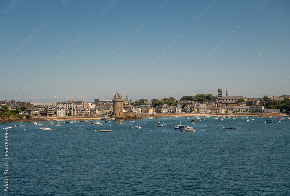 St. Malo, Brittany, France - July 8, 2022: Cityscape of Saint-Servan neighborhood at its beach on Rance river mouth with left the Solidor towers and right Sainte-Croix church under blue sky. Yachts.