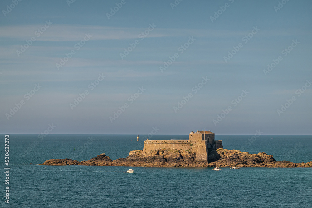 St. Malo, Brittany, France - July 8, 2022: closeup of brown stone Petit Be fort on its islet in front of old town set in English Channel under blue sky and darker blue water.