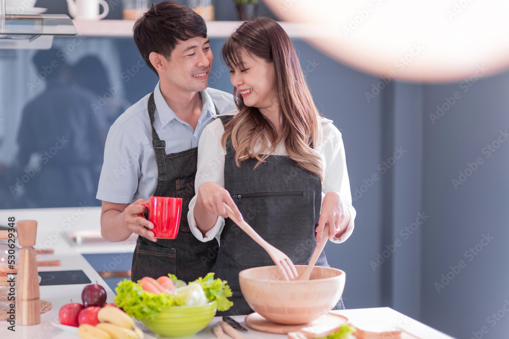 happy asian couple cooking healthy food. attractive wife and cheerful husband preparing delightful meal with fresh ingredients. fun married people make vegetable salad for dinner together in kitchen