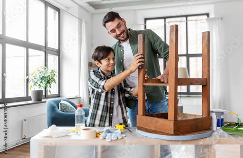 furniture renovation, diy and home improvement concept - father and son sanding old round wooden table with sponge at home