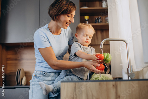 Woman with her son washing vegetables in the kitchen sink photo