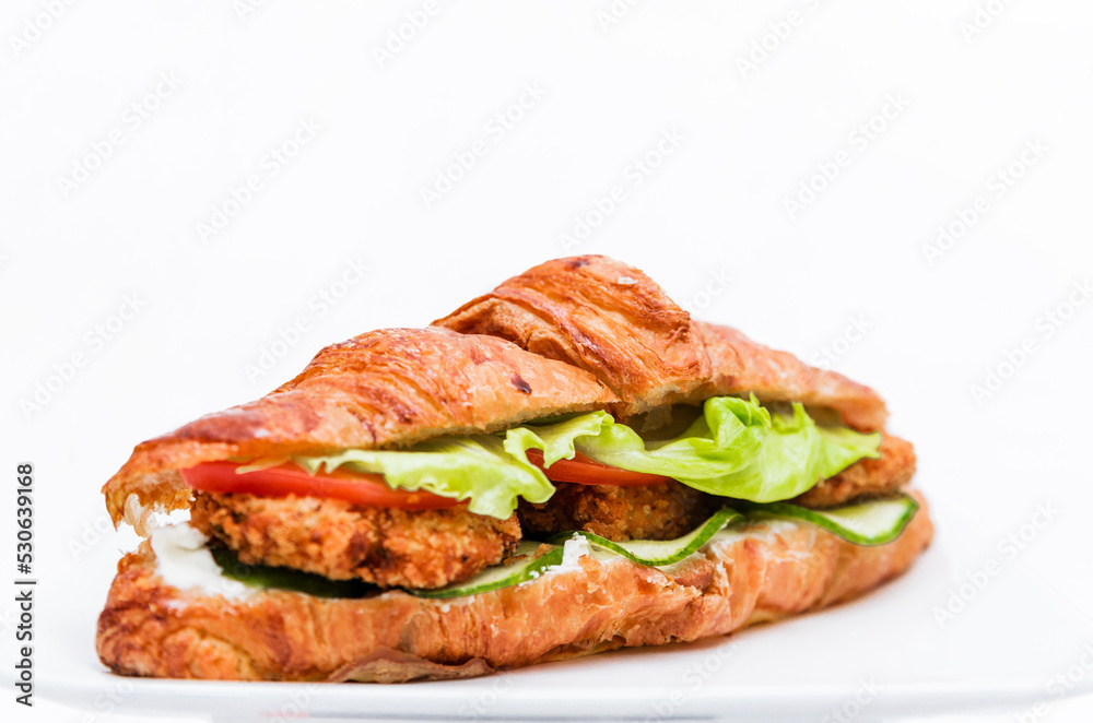 Croissant with chicken cutlet, fresh cucumber, tomato and lettuce on a white background.