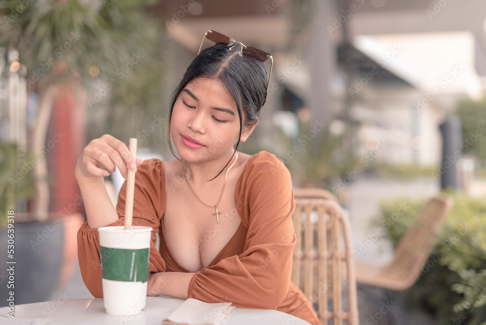 A young woman wearing a brown puffed long sleeved dress sits outside the cafe with her cold drink. A young woman wearing a brown puffed long sleeved dress sits outside the cafe with her cold drink.