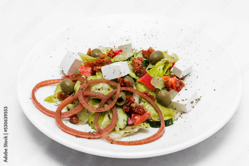 Salad with feta cheese, sun-dried tomatoes, pickled onions with balsamic sauce on a white plate.