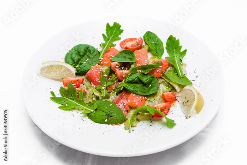 Salad with lightly salted trout, autocados, tomatoes, arugula, spinach and pesto sauce on a white plate.