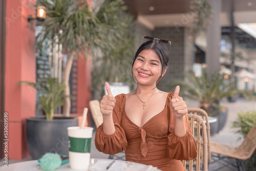 A smiling young woman poses for the camera while holding two thumbs up outside the cafe.