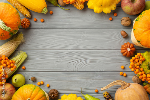 Thanksgiving day concept.. Top view photo of raw vegetables pumpkins maize pattypans zucchini apples pears walnuts rowan acorns on isolated grey wooden table background with copyspace in the middle photo