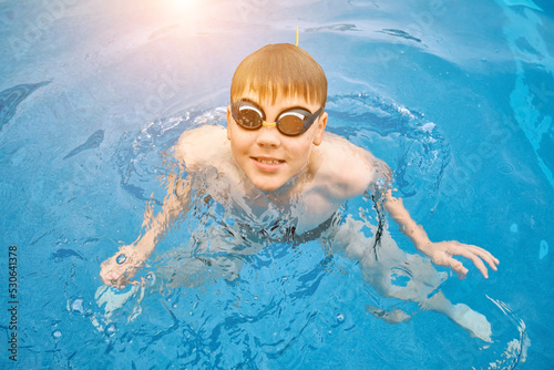 Smiling boy portrait in swimming goggles, Child swim in the pool, sunbathes, swimming in hot summer day. Relax, Travel, Holidays, Freedom concept. 4K slow motion
