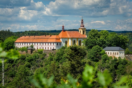 Rabstejn nad Strelou, Czech Republic - June 12 2022: View of the building of former monastery of Servites and the Virgin Mary church standing on a rock. Green trees in the foreground. Sunny summer day