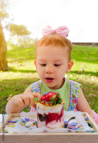 pretty red-haired girl looking at a strawberry cake during her birthday in the park