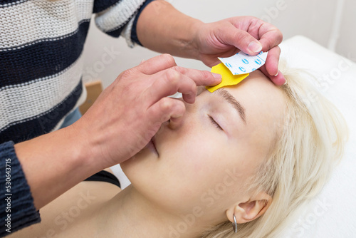 female cosmetician doing the taping of the face of the patient