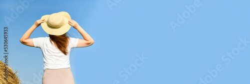 Back view of red-haired woman, girl in straw hat standing against the blue sky. Harvesting concept. Vacation concept. Banner