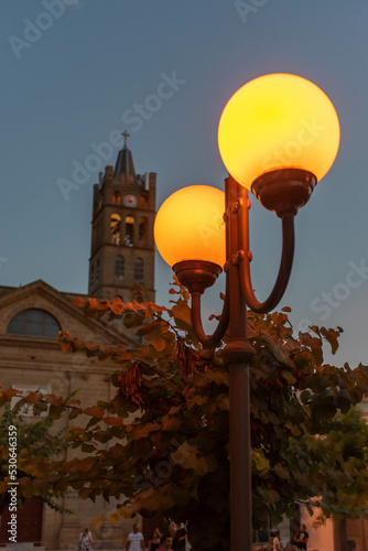 the bell tower of the mother church of Pulsano, in the province of Taranto, Italy, with a street lamp lit in the foreground at the blue hour on a blurred background photo