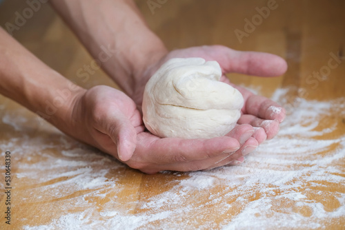 Lump of dough for pizza in the palms in the process of preparing the dough on the wooden table with flour on it
