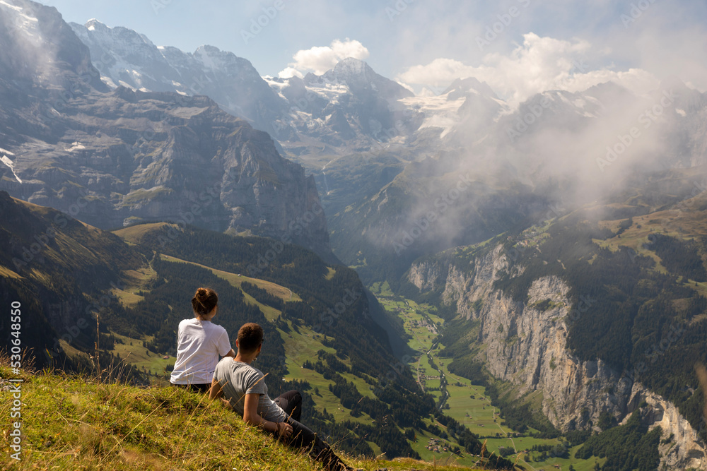 Couple of hikers in a valley of the Alps mountains of Switzerland enjoying the panoramic view