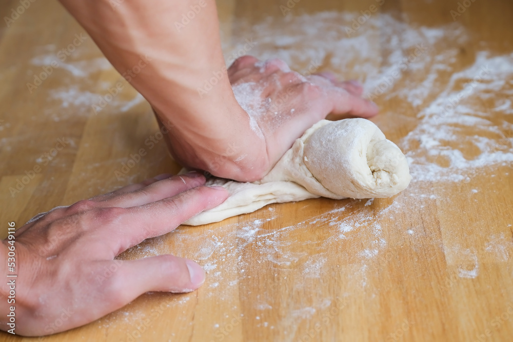 Hands kneading and crumpling dough on the wooden table with white flour closeup