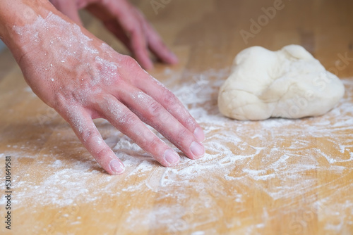 Hands in flour next to lump of dough on wooden board, person kneading dough