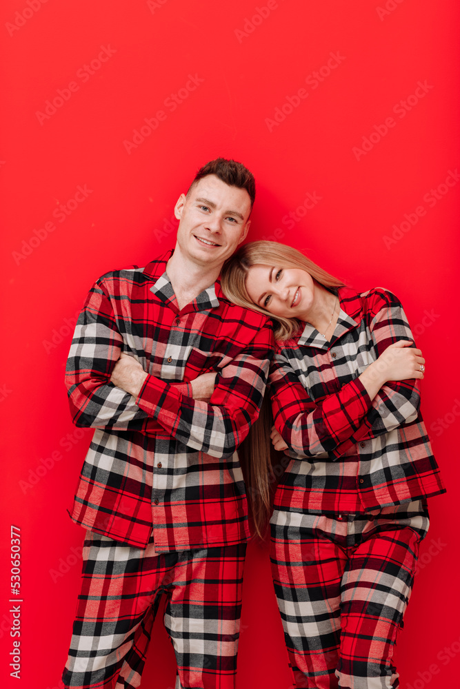 Happy Saint Valentine's Day. Smiling young couple in the same pyjamas having fun on red background. Man and woman in love are enjoying spending time together while celebrating. Happy Saint Valentine's Day. Smiling young couple in the same pyjamas having fun on red background. Man and woman in love are enjoying spending time together while celebrating.