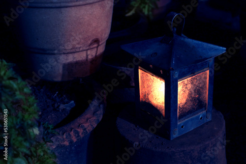 Obraz na plátně An oily garden lamp shines in the dark near pots with tulasi plants