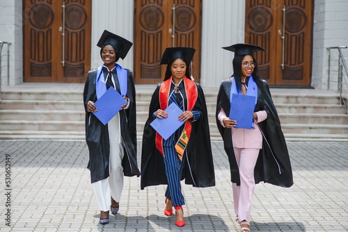 education, graduation and people concept - group of happy international graduate students in mortar boards and bachelor gowns with diplomas