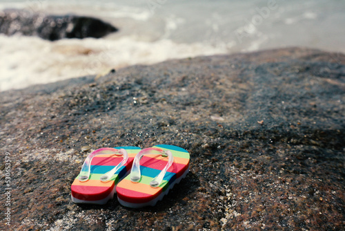 Beach striped slippers on a stone by the sea. © d_odin