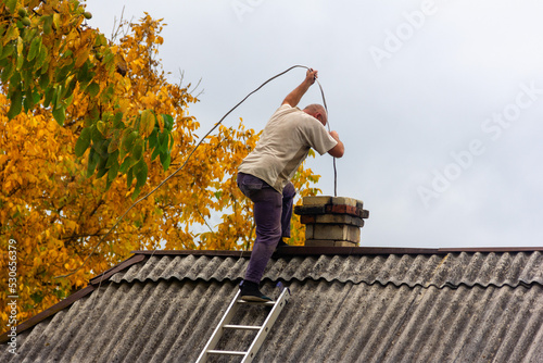 Konstfotografi a male chimney sweep cleans the chimney from soot on the roof of a village house