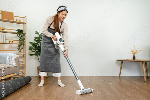 Housekeeper is use mop with vacuum cleaner to housekeeping with vacuuming and wiping dirty laminate on the floor in living room while working to perform routine house cleaning