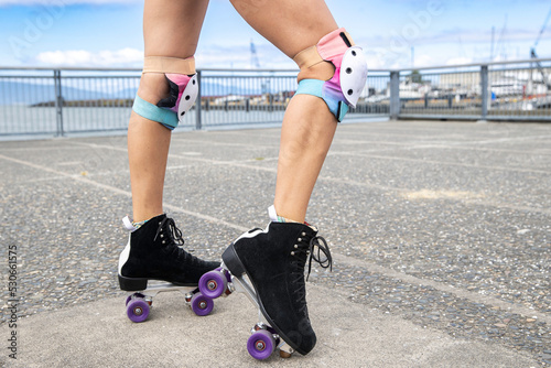 Close up view of woman legs wearing roller skates with wheels and knee pads for safety and protection while having fun at the park. 