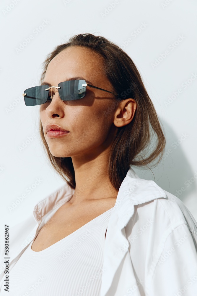 A beautiful woman model with tanned skin and a beautiful slender body wearing sunglasses poses against a white background. Body care and skin health concept with spf A beautiful woman model with tanned skin and a beautiful slender body wearing sunglasses poses against a white background. Body care and skin health concept with spf