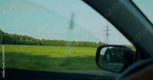 Sunny summer day, a view of a dense forest, a green sunny meadow from the car window, a view through the side glass.