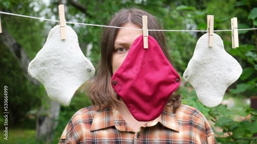 Womens period and health care concept. Portrait of middle age woman with hanged reusable cloth sanitary menstrual pads to dry on clothesline. Feminine washable, eco friendly personal hygiene supplies.