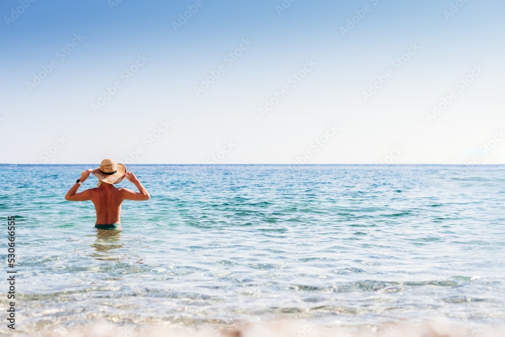 Beautiful blond woman in a straw hat standing back in the sea on a beach in Corfu, Greece