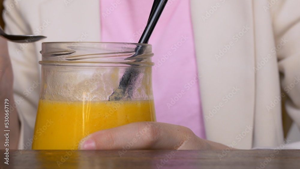 Close-up shot of a delicious yellow smoothie being eaten from a glass beaker. A woman in a cafe eats a mango smoothie with a spoon. Healthy organic fruit smoothie with lots of vitamins. Close-up shot of a delicious yellow smoothie being eaten from a glass beaker. A woman in a cafe eats a mango smoothie with a spoon. Healthy organic fruit smoothie with lots of vitamins.